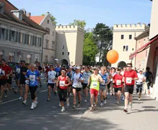 Un grupo de corredores con ropa deportiva corriendo por una calle de la ciudad, algunos sosteniendo un globo naranja.