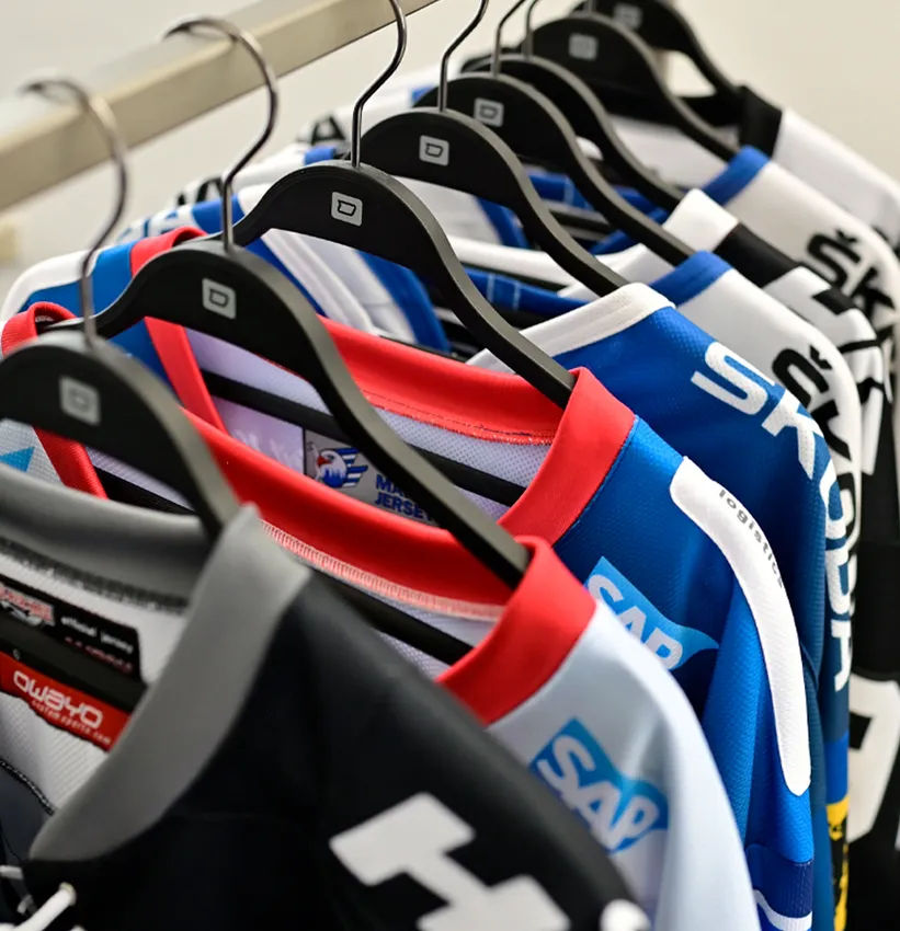 Una fila de camisetas deportivas coloridas personalizadas de owayo cuelgan de perchas negras en un perchero.