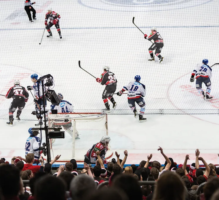 Una escena dinámica de hockey sobre hielo con jugadores en acción sobre el hielo y una multitud animada de fondo.