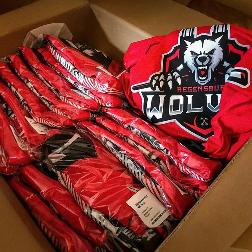 Una caja llena de ropa deportiva roja con un logo de lobo y varios artículos de ropa envueltos en plástico transparente.