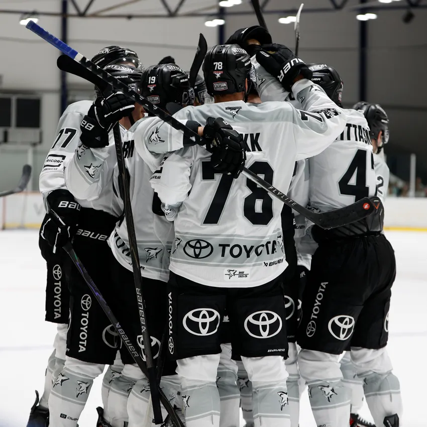 Un grupo de jugadores de hockey sobre hielo con camisetas blancas se abrazan sobre el hielo después de anotar un gol.