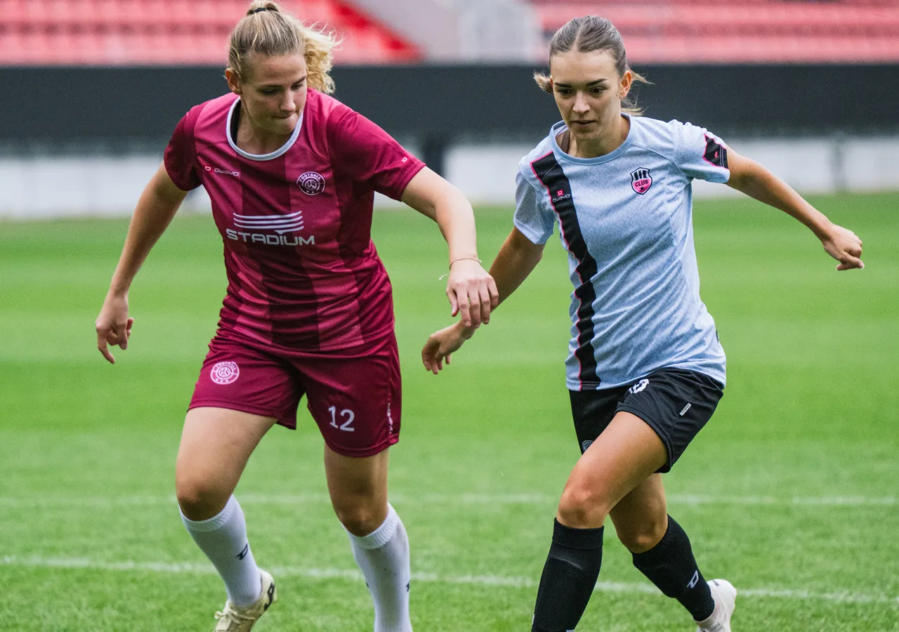 Dos mujeres con ropa deportiva están jugando al fútbol en un campo de hierba.