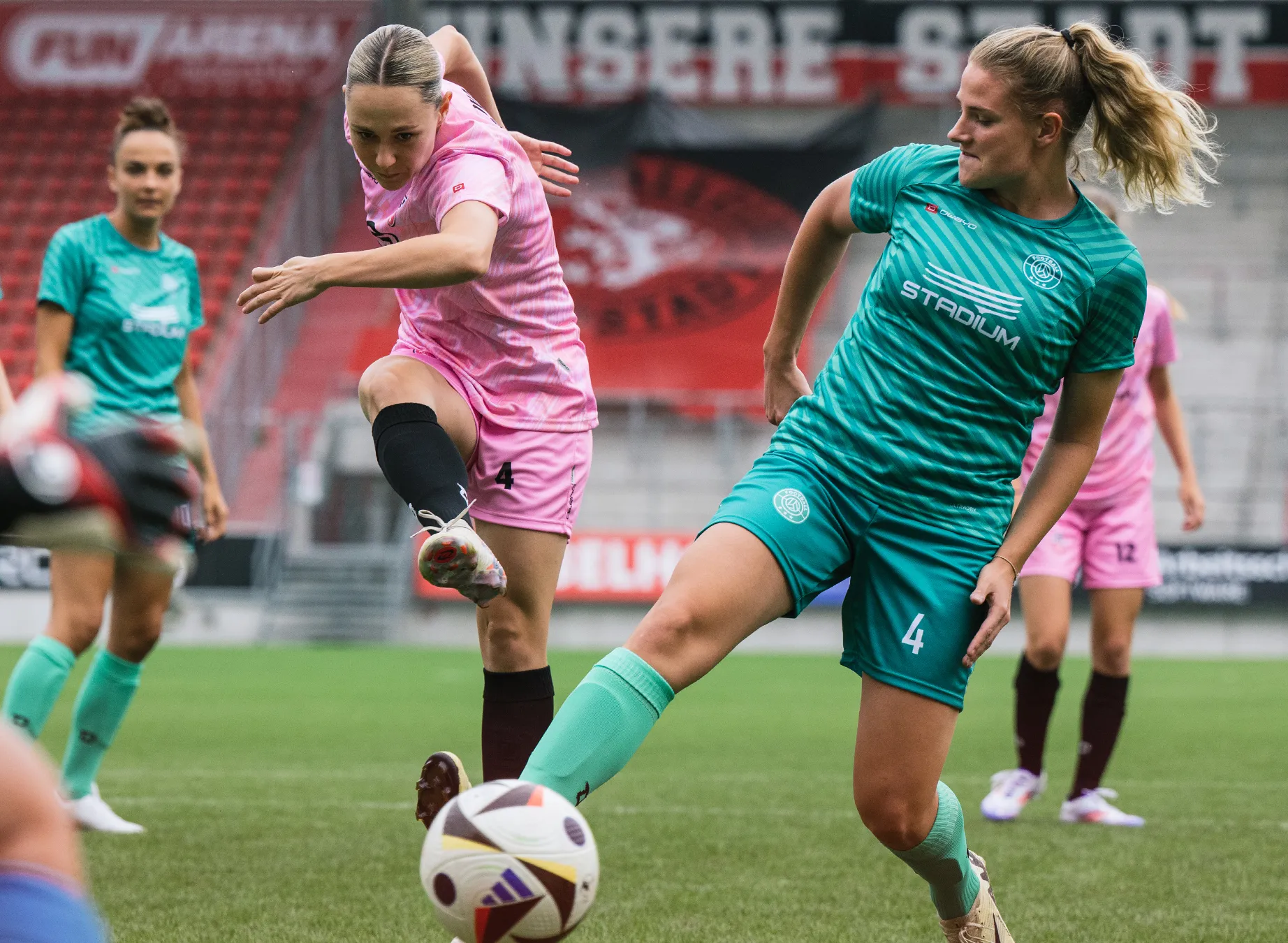 Dos mujeres en camisetas deportivas coloridas están jugando al fútbol en un campo de hierba.