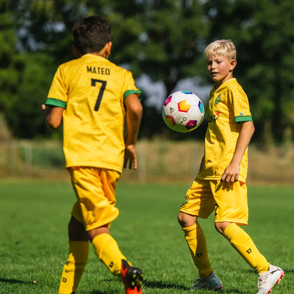 Dos niños con camisetas y pantalones cortos de fútbol amarillos juegan en un campo de fútbol verde.