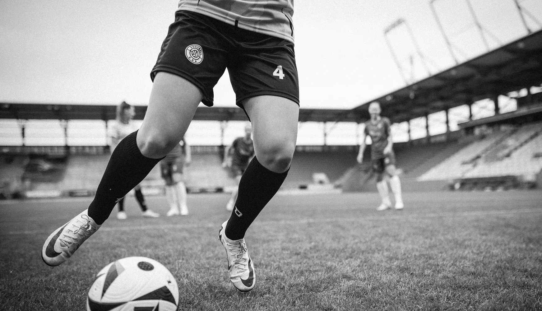 Una jugadora con pantalones cortos de fútbol y calcetas largas patea un balón en un campo de fútbol.