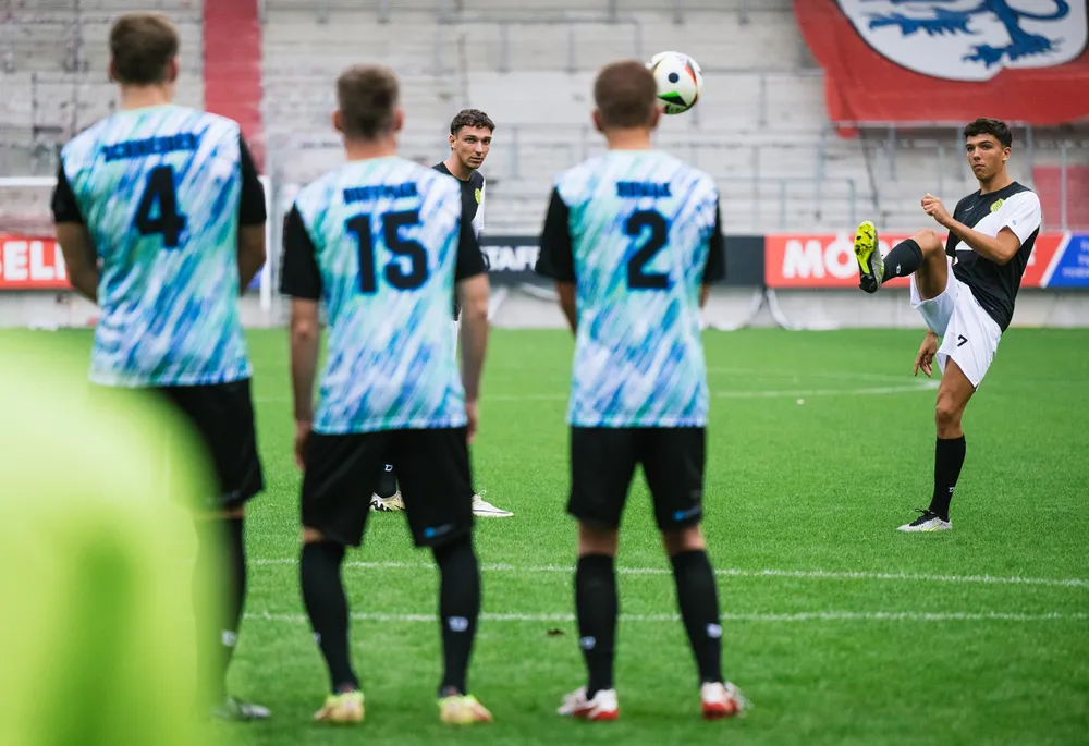 Un grupo de futbolistas con camisetas coloridas está en el campo mientras un jugador se prepara para ejecutar un tiro libre.