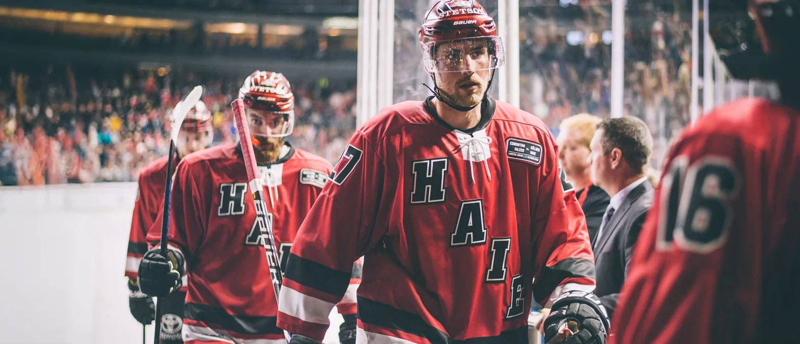 Jugadores de hockey sobre hielo con camisetas rojas con las letras 'H', 'A', 'I', 'E' y el número 7 en la espalda, de pie sobre el hielo.