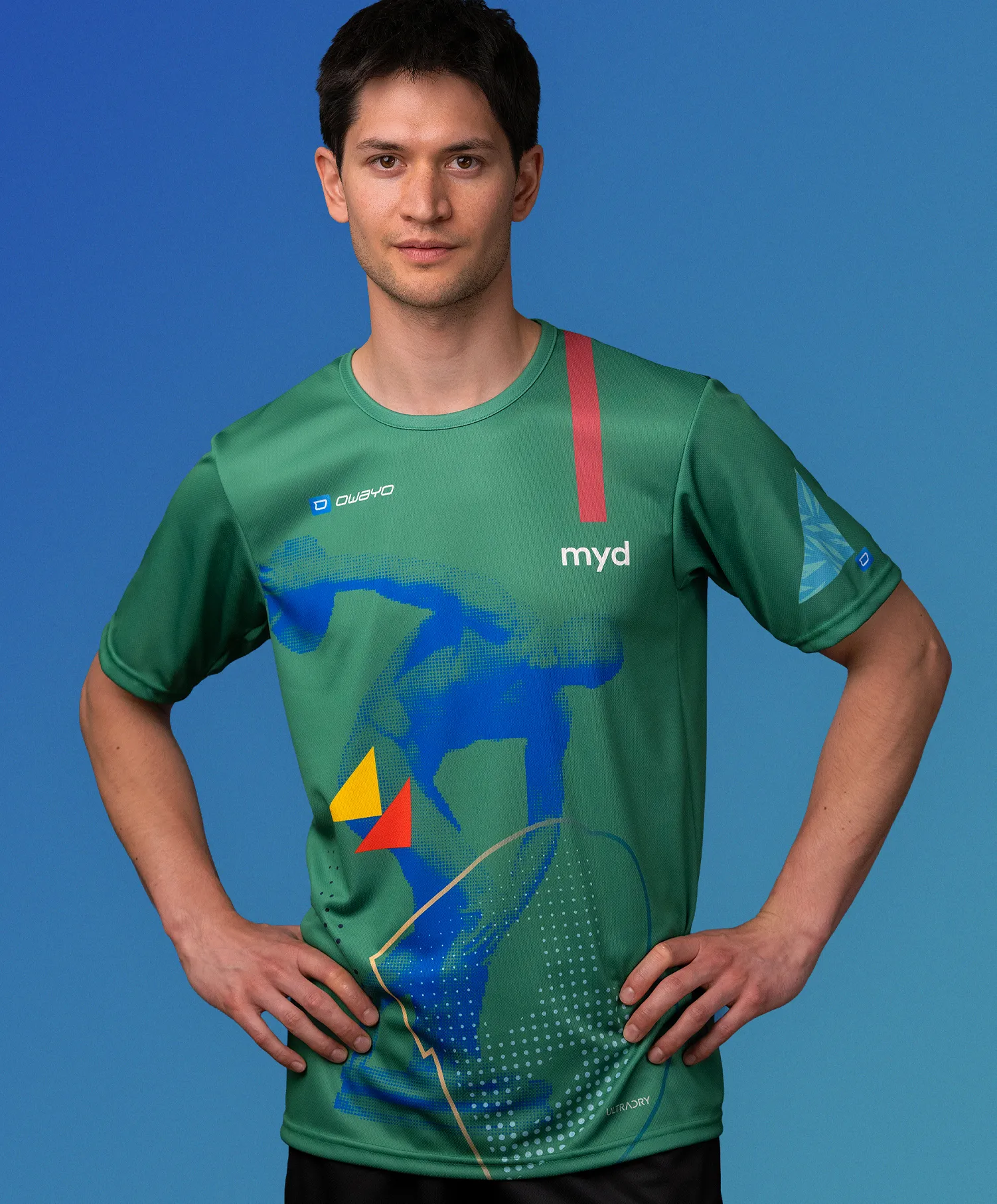 Un hombre vistiendo una camiseta deportiva verde personalizada de owayo con un diseño gráfico azul, amarillo y rojo y la palabra 'myd' en el pecho.