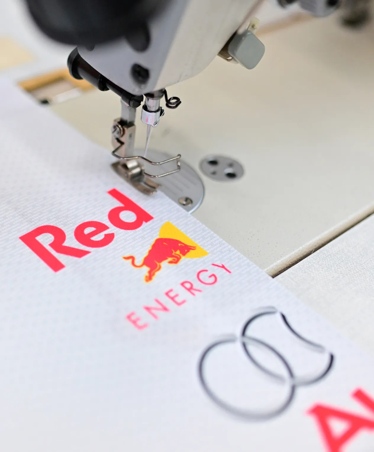 Una máquina de coser está cosiendo una prenda deportiva blanca con el logotipo de Red Bull Energy.