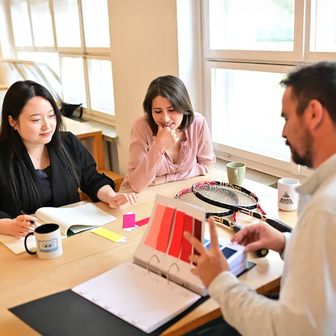 Tres personas están sentadas en una mesa discutiendo paletas de colores y diseños para ropa deportiva personalizada.