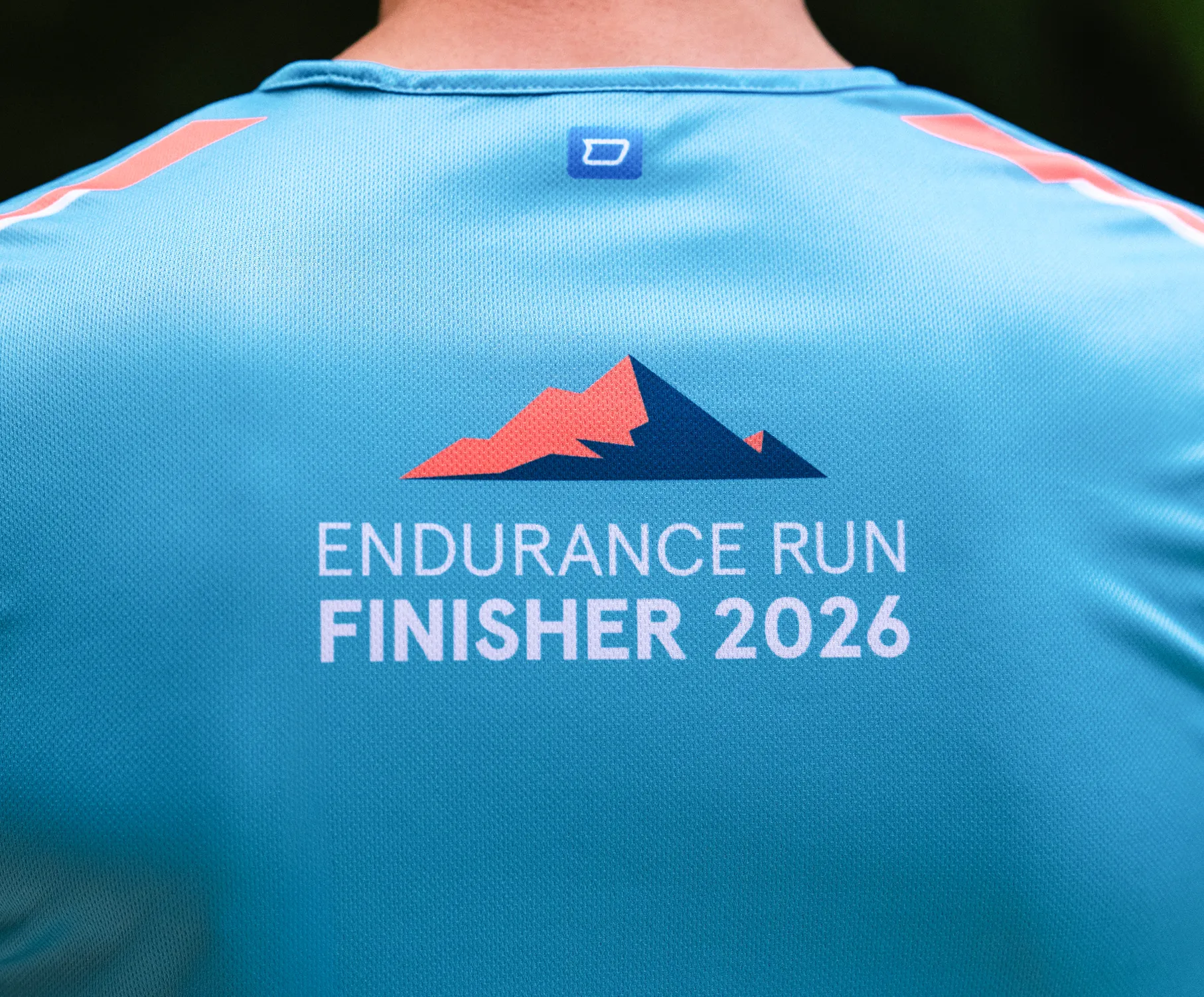 Una camiseta deportiva azul con la impresión 'ENDURANCE RUN FINISHER 2026' y un diseño de montaña estilizado en la parte posterior.