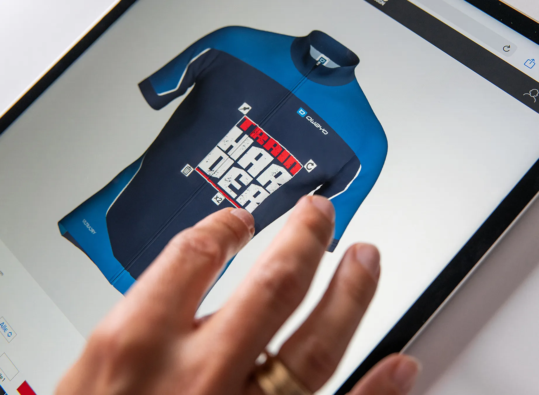 Una mano señala un diseño digital de una camiseta deportiva azul con el texto 'train harder'.