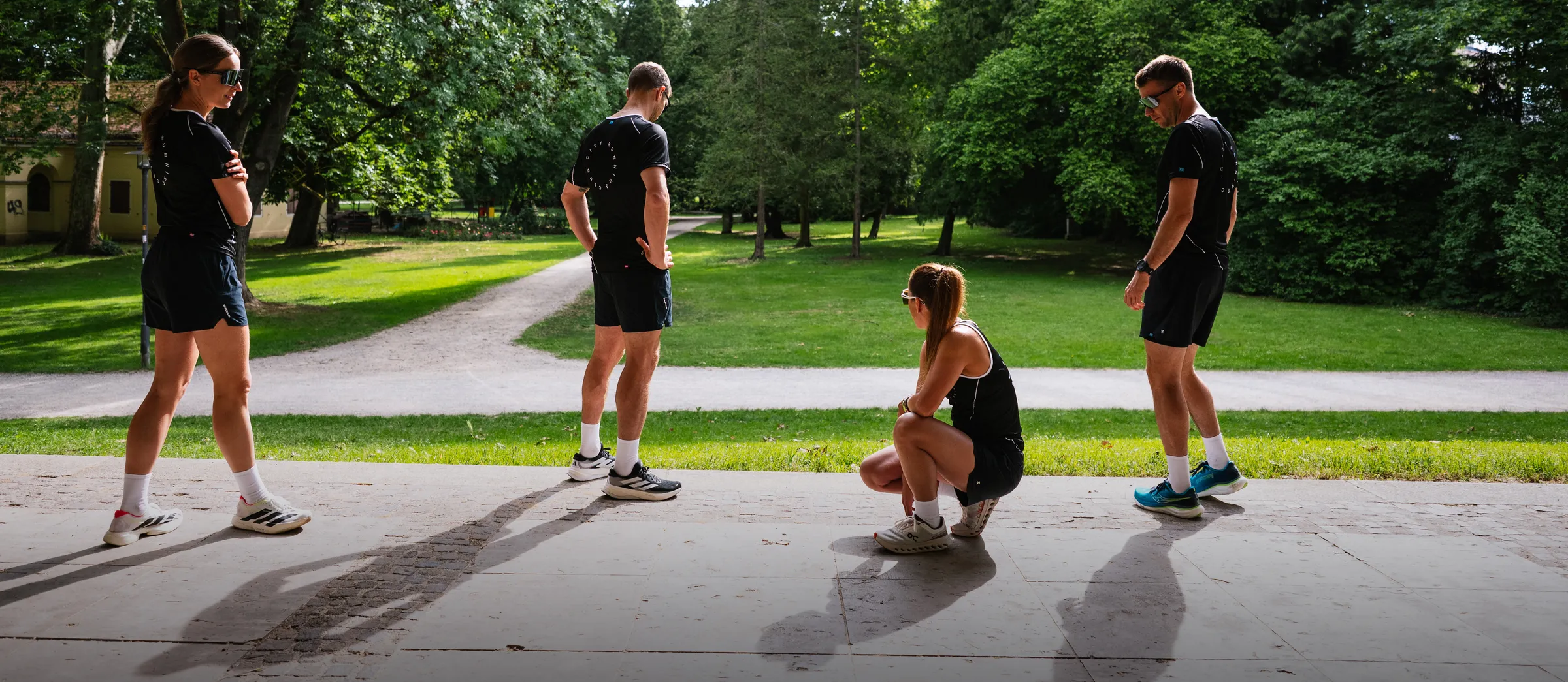 Cuatro personas con ropa deportiva están de pie y sentadas en un paisaje de parque verde.