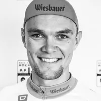 Un hombre con un traje de ciclismo con el logotipo 'Wiesbauer' en la gorra y la camiseta.