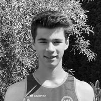 Un joven con una camiseta deportiva sin mangas negra y gris con el logo 'owayo' en el pecho, sonriendo frente a un fondo de hojas verdes.