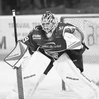 Un portero de hockey sobre hielo con equipo completo, incluyendo casco, máscara, guantes y protectores de piernas, está en posición defensiva sobre el hielo.