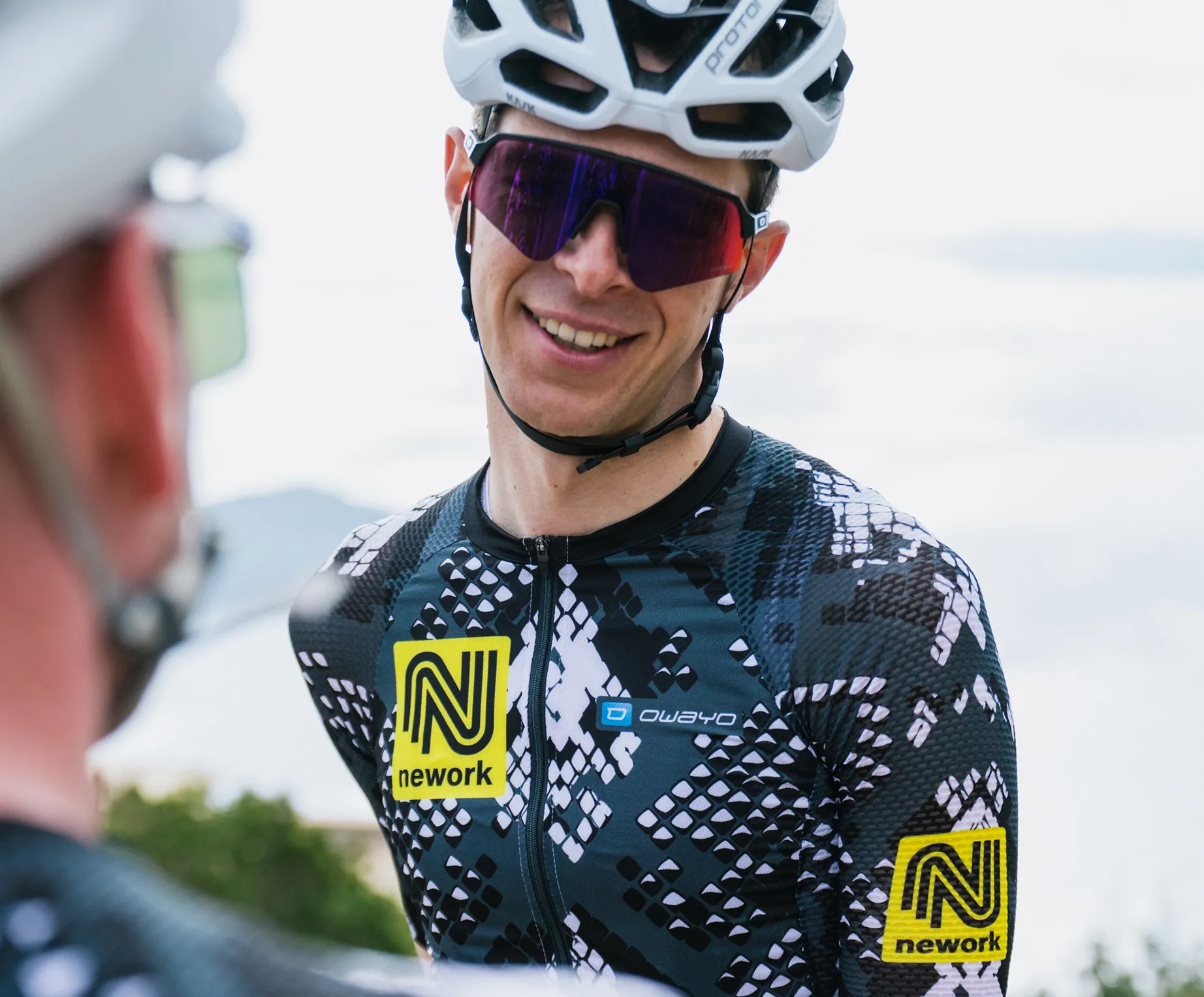 Un ciclista lleva una camiseta personalizada con estampado negro y blanco, con un logo amarillo de 'nework' y un logo de 'owayo' en el pecho.