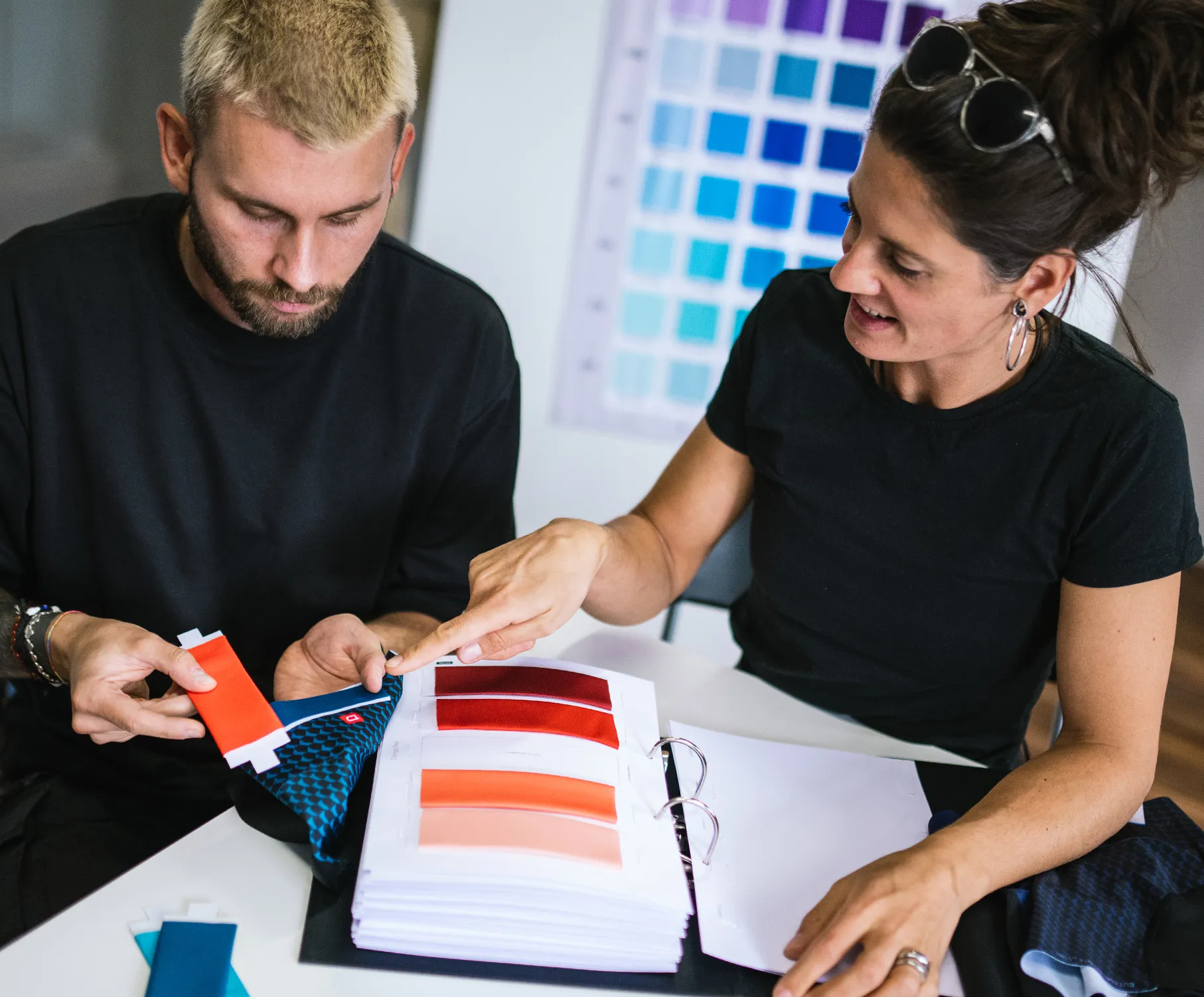 Un hombre y una mujer seleccionan colores para ropa deportiva personalizada, examinando muestras de tejidos y paletas de colores.