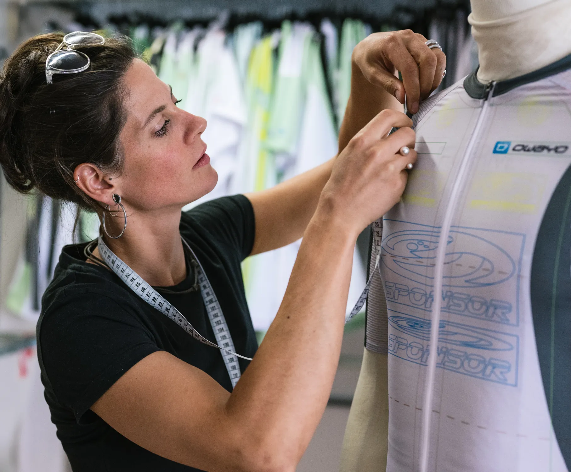 Una mujer ajusta una camiseta deportiva personalizada en un maniquí, llevando una cinta métrica alrededor del cuello.