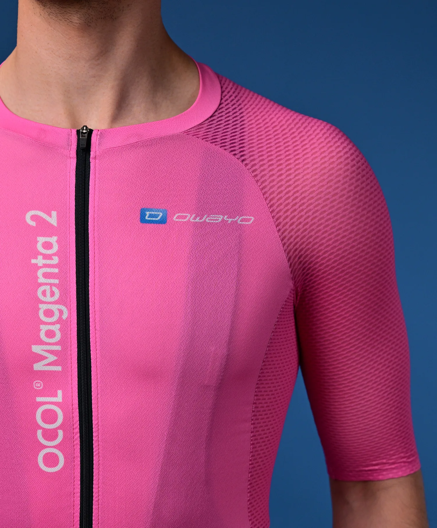 Un hombre lleva una camiseta de ciclismo rosa de manga corta con una cremallera negra y el logotipo 'owayo' en el pecho. Verticalmente en el lado izquierdo dice 'OCOL Magenta 2'.
