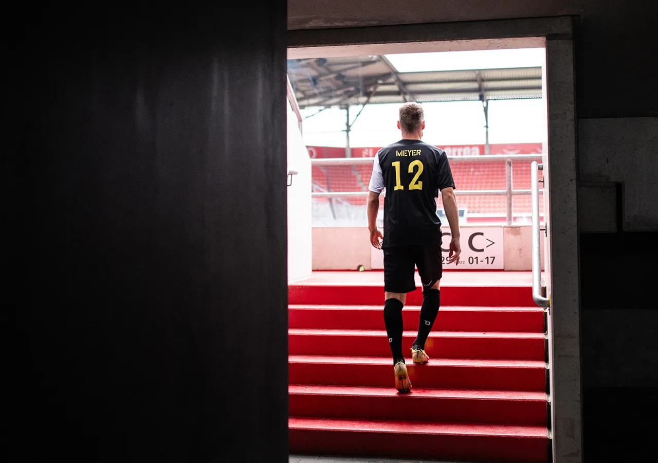 Un futbolista con el nombre Meyer y el número 12 en la espalda sube una escalera roja hacia un estadio.